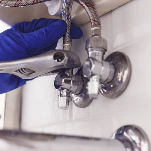 Plumber turns nut on angle valve under wash basin using spreading wrench