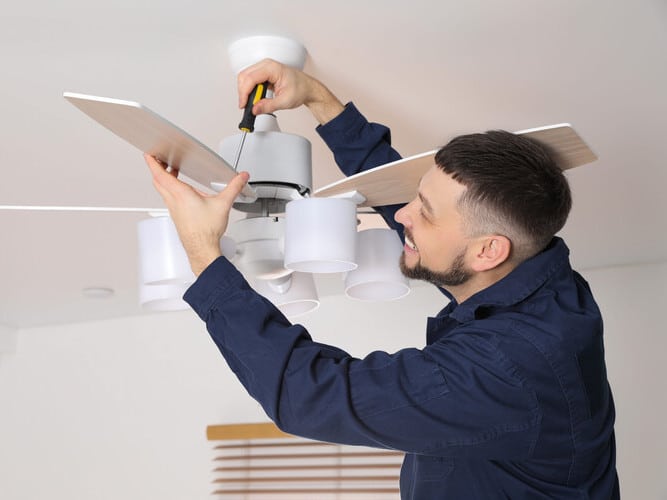 Electrician with screwdriver repairing ceiling fan indoors