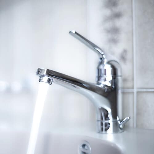 Shiny, chrome faucet with running water stream inside apartment bathroom. Close up shot, shallow depth of field, no people
