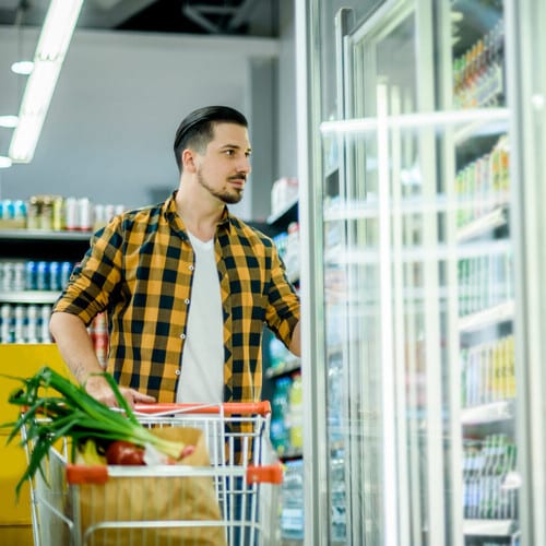 Young handsome man in a supermarket choosing products from a walk-in cooler